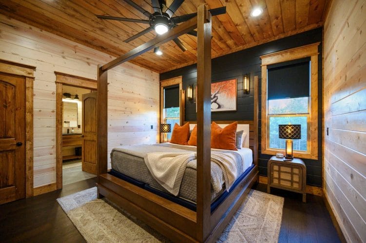 Bed with a wood four-post frame, orange pillows and a window beside a dark shiplap wall