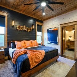 Bed with orange pillows and a blue blanket in front of a dark shiplap wall and a window