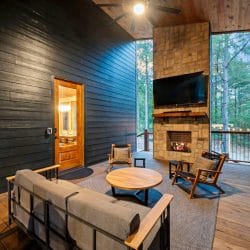Covered porch with a rocking chair beside the outdoor stone fireplace and a TV