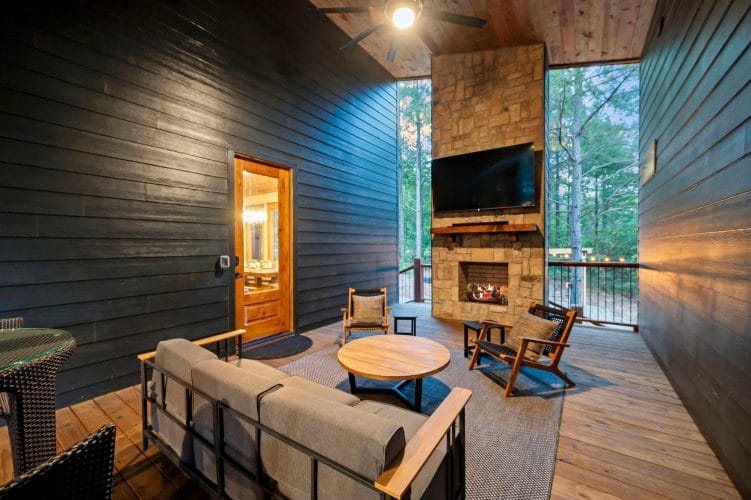 Covered porch with a rocking chair beside the outdoor stone fireplace and a TV