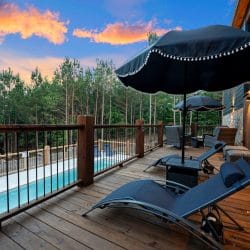 Wood pool deck with a railing, patio umbrella and loungers above the pool