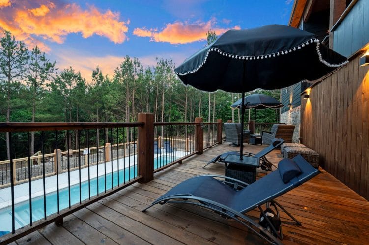Wood pool deck with a railing, patio umbrella and loungers above the pool