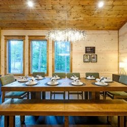 Dining table place settings beside a tall window with pine trees outside