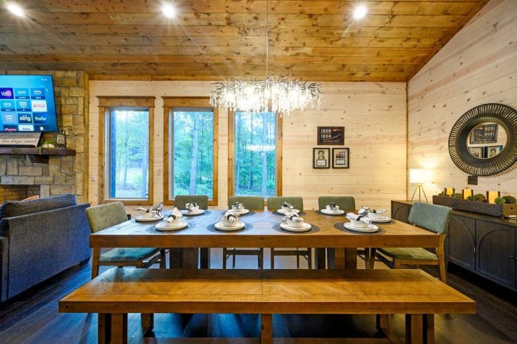 Dining table place settings beside a tall window with pine trees outside