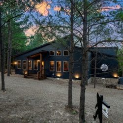 Dark blue-gray cabin siding with lit windows and exterior lights at dusk