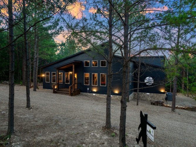 Dark blue-gray cabin siding with lit windows and exterior lights at dusk