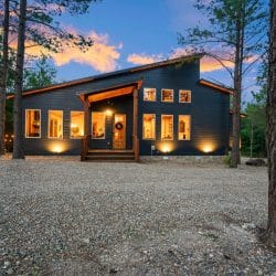 Front of the cabin at dusk with lit windows, wreath on the door and a gravel drive