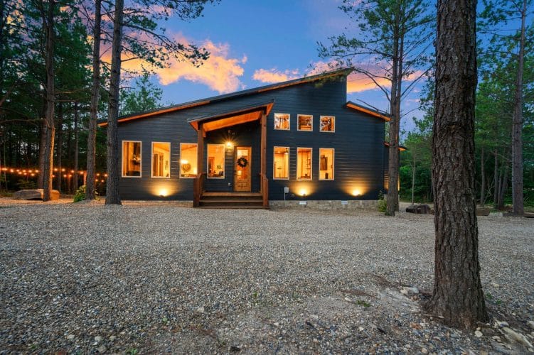 Front of the cabin at dusk with lit windows, wreath on the door and a gravel drive