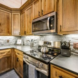 Stovetop, range hood and kitchen utensils against a light stone backsplash
