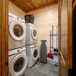 Stacked washer and dryer with an ironing board and mop on the wall