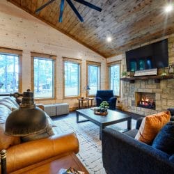 Living room corner with a blue armchair, ottomans and tall windows looking at the pines