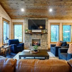 Stone fireplace with a lit gas log, wood mantel and TV above it