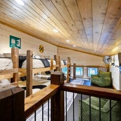 Loft with stacked bunk-style beds, a railroad crossing sign on the wall and a wood railing overlooking the room below