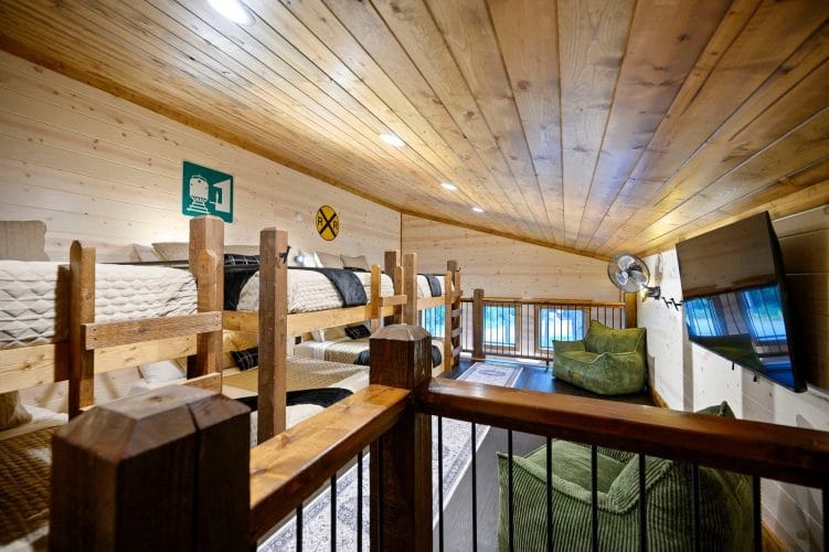 Loft with stacked bunk-style beds, a railroad crossing sign on the wall and a wood railing overlooking the room below