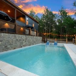 Pool at dusk with blue in-pool loungers, deck railing and string lights