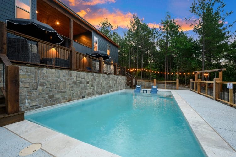 Pool at dusk with blue in-pool loungers, deck railing and string lights