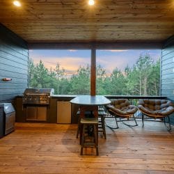 Deck bar counter and a round woven chair looking out at pine trees at sunset