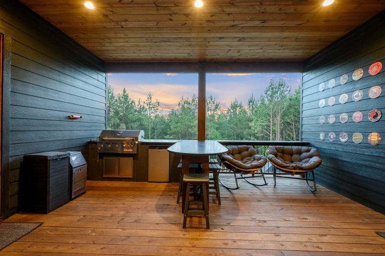 Deck bar counter and a round woven chair looking out at pine trees at sunset
