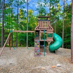 Wooden playset with climbing wall, swings and a green slide in the trees