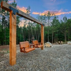 Wooden swing benches under a post-and-beam frame with the playset behind