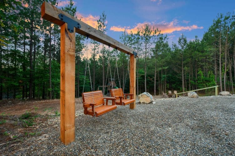 Wooden swing benches under a post-and-beam frame with the playset behind