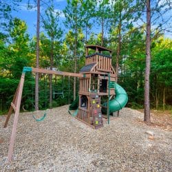 Wooden playset with a green spiral slide, swings and climbing wall