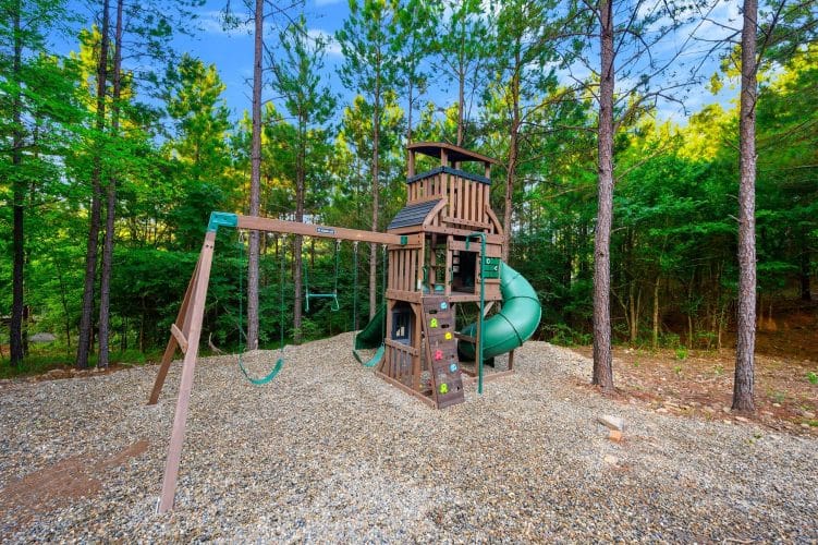 Wooden playset with a green spiral slide, swings and climbing wall