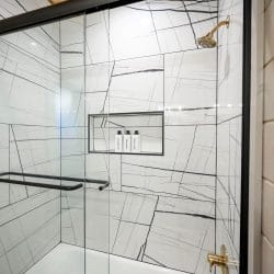 Shower with veined white tile and a built-in shelf with bottles
