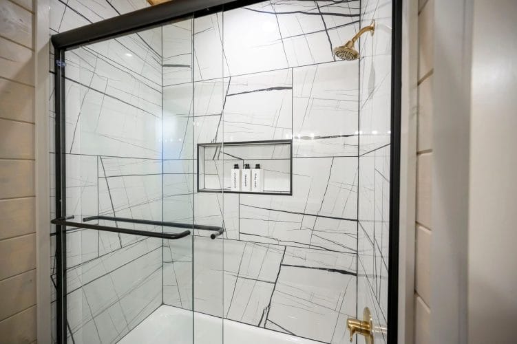 Shower with veined white tile and a built-in shelf with bottles