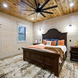 King bed with a dark carved headboard, orange bedding and a ceiling fan