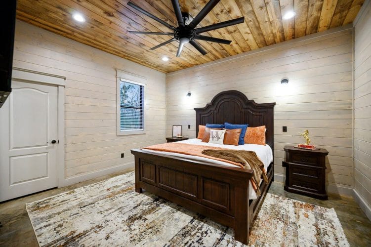 King bed with a dark carved headboard, orange bedding and a ceiling fan