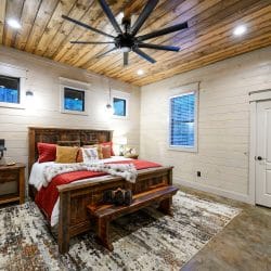 King bed with a rustic frame, red bedding and a bench, small high windows above