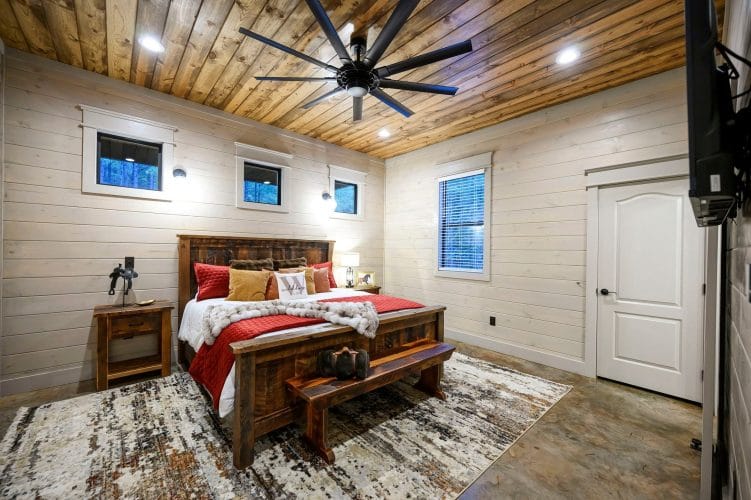 King bed with a rustic frame, red bedding and a bench, small high windows above