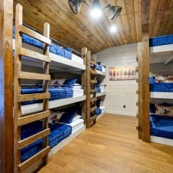 Large bunk room with four sets of triple-stacked bunks made up in blue bedding
