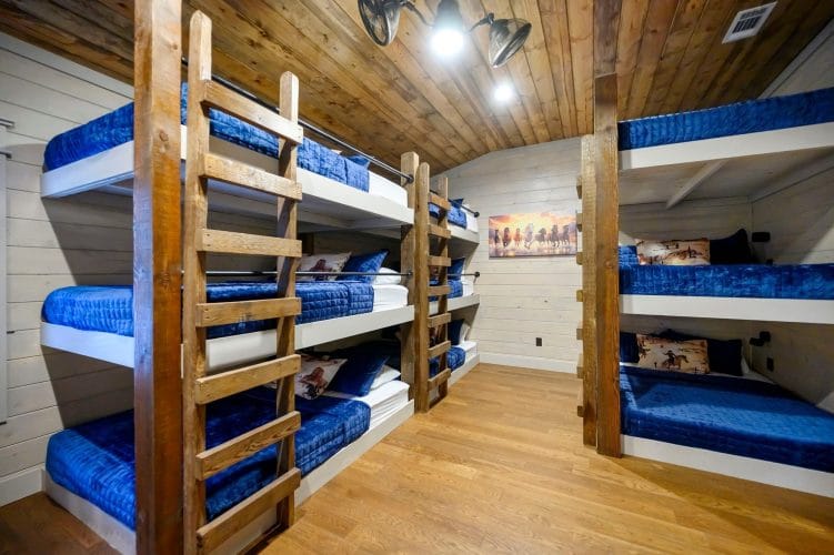Large bunk room with four sets of triple-stacked bunks made up in blue bedding