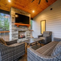 Covered patio with wicker chairs around a stone fireplace and TV