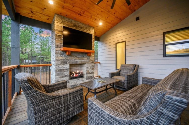 Covered patio with wicker chairs around a stone fireplace and TV