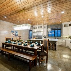 Long dining table with benches and chairs set for a meal, kitchen behind