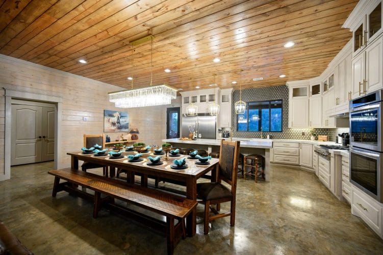 Long dining table with benches and chairs set for a meal, kitchen behind
