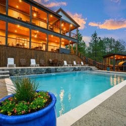 Multi-level lodge with stacked decks lit up at dusk, with the pool in the foreground