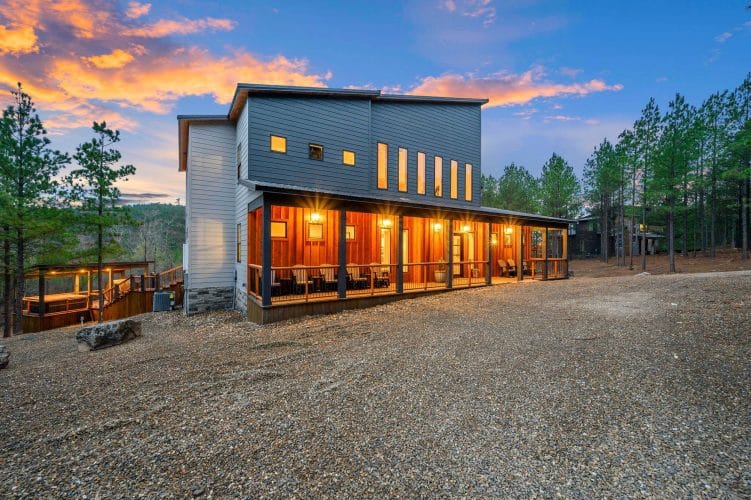 Back of the lodge with lit windows seen across the gravel lot at dusk