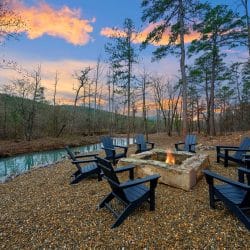 Stone fire pit with black Adirondack chairs on the bank of the creek