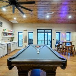 Pool table in the game loft with bar stools and sliding glass doors behind it