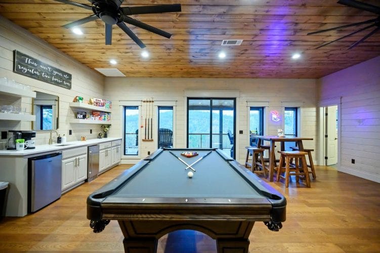 Pool table in the game loft with bar stools and sliding glass doors behind it