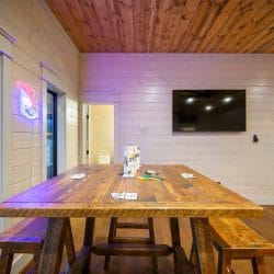 Wooden table with benches under a TV, a neon sign by the window