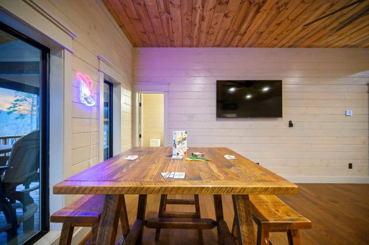 Wooden table with benches under a TV, a neon sign by the window