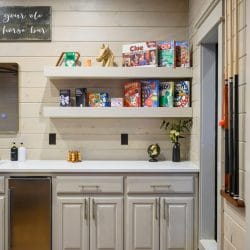 Wet bar with a mini fridge, cereal on floating shelves and cue sticks on the wall