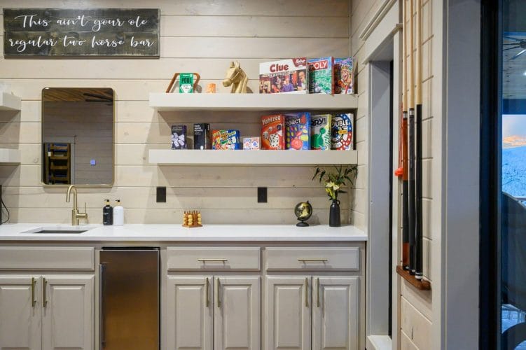 Wet bar with a mini fridge, cereal on floating shelves and cue sticks on the wall