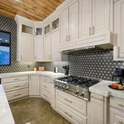Gas range under a hood with a patterned tile backsplash and white cabinets