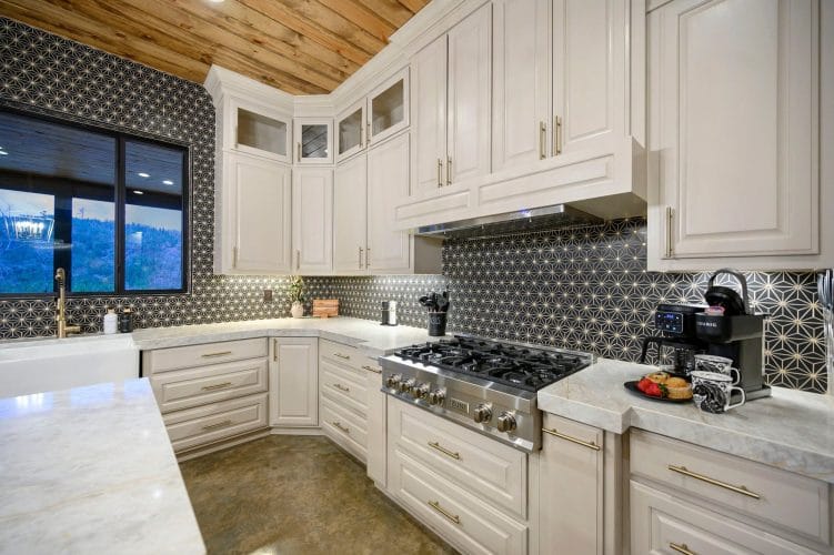 Gas range under a hood with a patterned tile backsplash and white cabinets